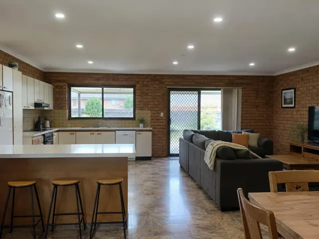 Open-plan kitchen and living room with recessed LED downlights in a brick-walled home in Kotara